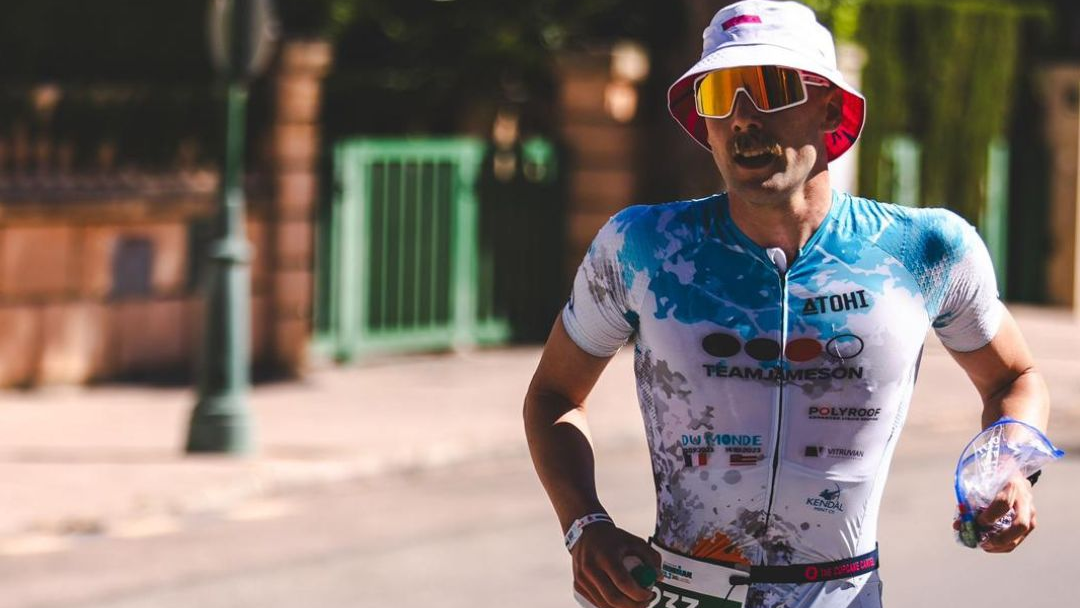 Fraser Minnican wearing a colorful cycling outfit with visible kendal mint co branding in an outdoor setting running an ironman event